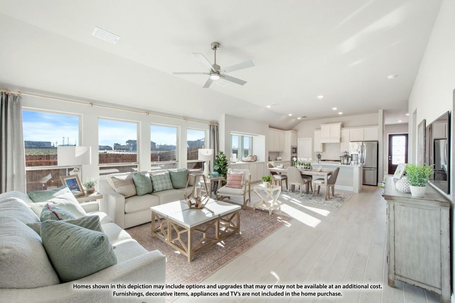 Open-concept living room with ceiling fan, light wood floors, and kitchen visible in background Open-concept living room with ceiling fan, light wood floors, and kitchen visible in background