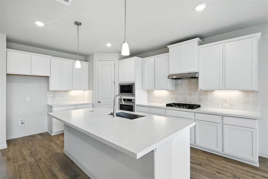 Kitchen with dark wood-style flooring, light countertops, backsplash, white cabinets, and decorative light fixtures