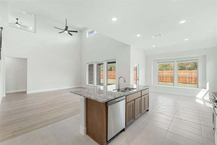 Kitchen island with granite countertop, sink, and dishwasher in open-concept space with vaulted ceiling and tile floors
