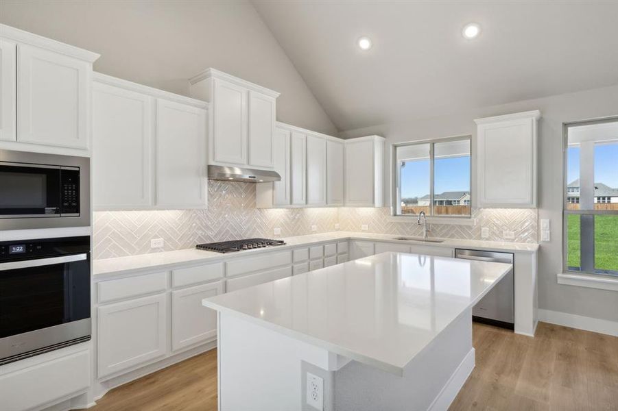 Kitchen with lofted ceiling, light hardwood / wood-style flooring, a kitchen island, white cabinetry, and stainless steel appliances