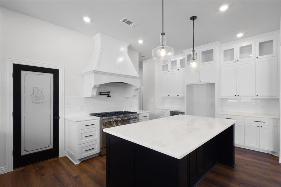 Kitchen with decorative backsplash, premium range hood, stainless steel stove, and visible vents