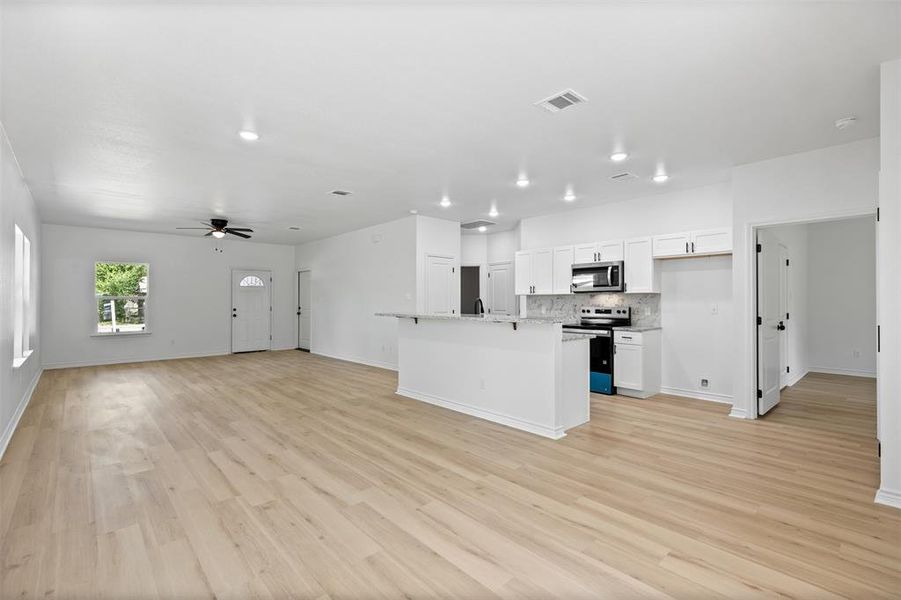 Kitchen with open floor plan, white cabinetry, appliances with stainless steel finishes, light wood-style flooring, and a kitchen island with sink