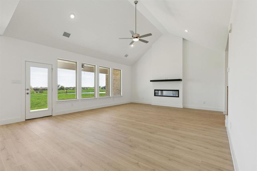 Unfurnished living room featuring a glass covered fireplace, high vaulted ceiling, light wood-style floors, recessed lighting, and ceiling fan