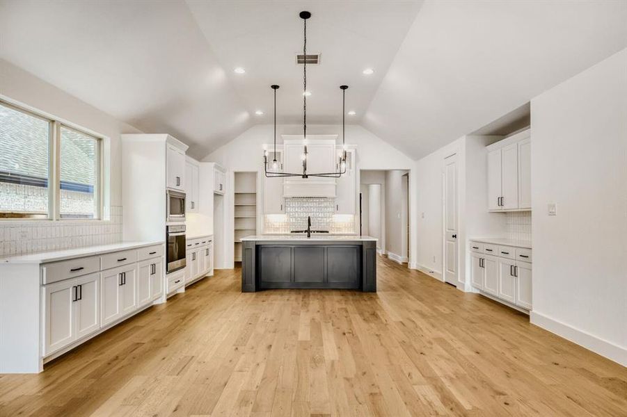 Kitchen featuring backsplash, a kitchen island with sink, two tone cabinetry, light wood-type flooring, and stainless steel appliances