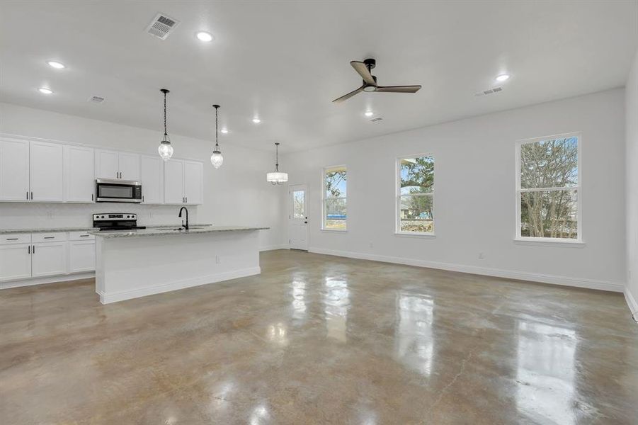 Kitchen with finished concrete floors, a center island with sink, hanging light fixtures, white cabinets, and a ceiling fan