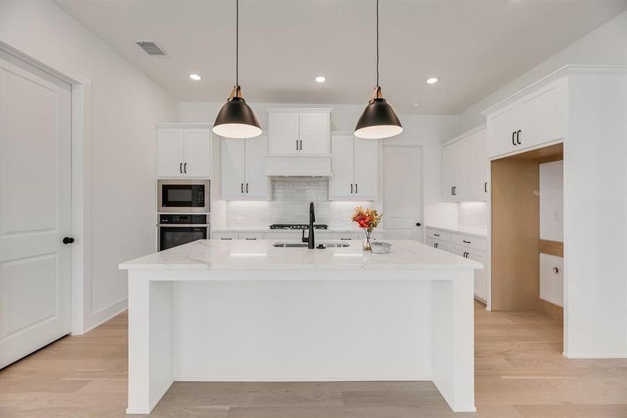 Kitchen with white cabinets, tasteful backsplash, light wood finished floors, light stone counters, and pendant lighting Kitchen with white cabinets, tasteful backsplash, light wood finished floors, light stone counters, and pendant lighting