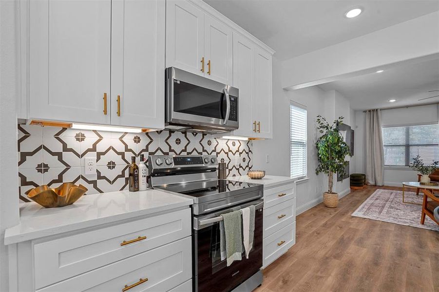 Kitchen with light stone countertops, light wood-type flooring, stainless steel appliances, white cabinets, and decorative backsplash