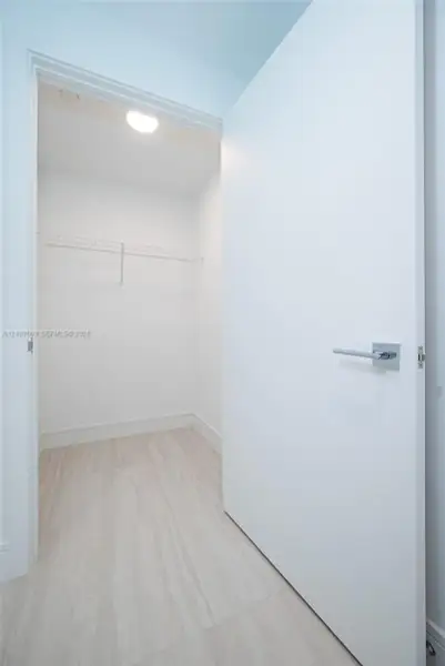 Walk-in storage space featuring wood-finish flooring, a white flat-panel door with a square-back plate lever handle, and a mounted wire shelving system