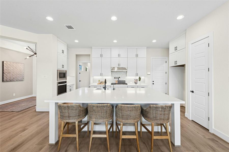 Kitchen featuring a breakfast bar, decorative backsplash, white cabinets, recessed lighting, and a center island with sink Kitchen featuring a breakfast bar, decorative backsplash, white cabinets, recessed lighting, and a center island with sink