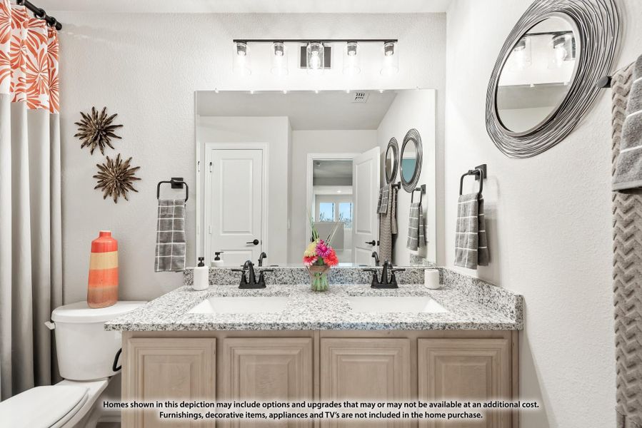Bathroom with double sink vanity, granite countertops, large mirror, and light wood cabinets