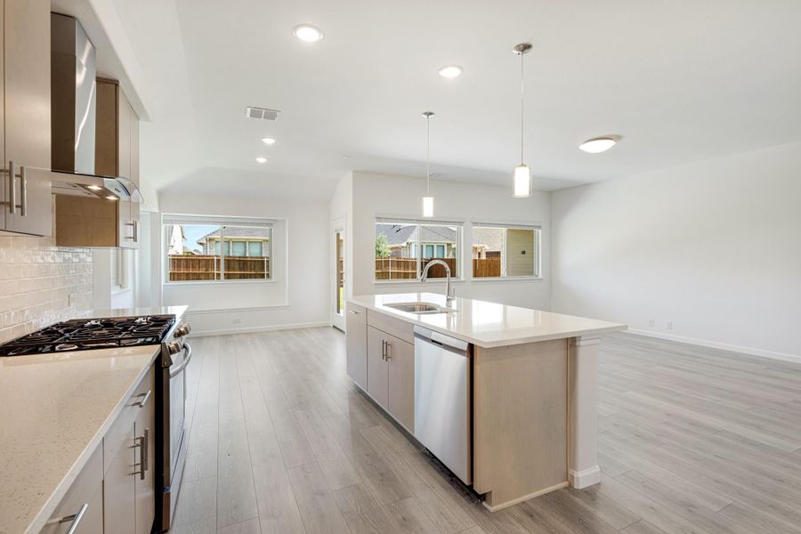 Open kitchen with center island, stainless steel appliances, pendant lights, and light wood floors opening to living area Open kitchen with center island, stainless steel appliances, pendant lights, and light wood floors opening to living area
