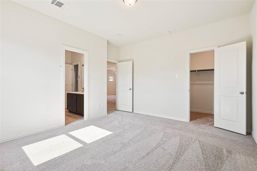 Unfurnished bedroom featuring a spacious closet, ensuite bath, a closet, and light colored carpet