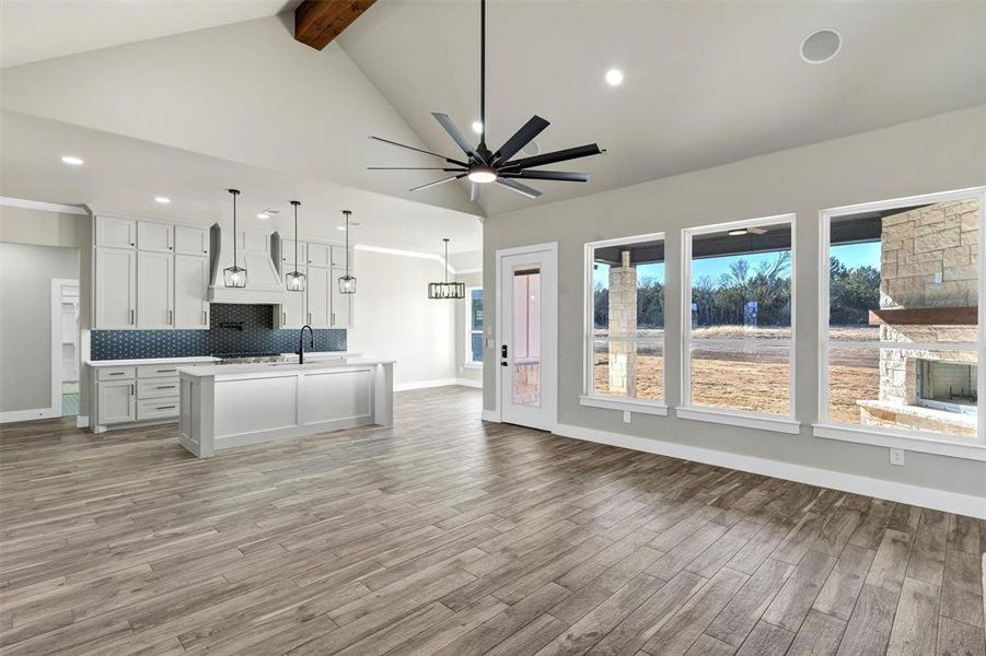 Kitchen featuring white cabinetry, hanging light fixtures, a kitchen island with sink, lofted ceiling with beams, and decorative backsplash