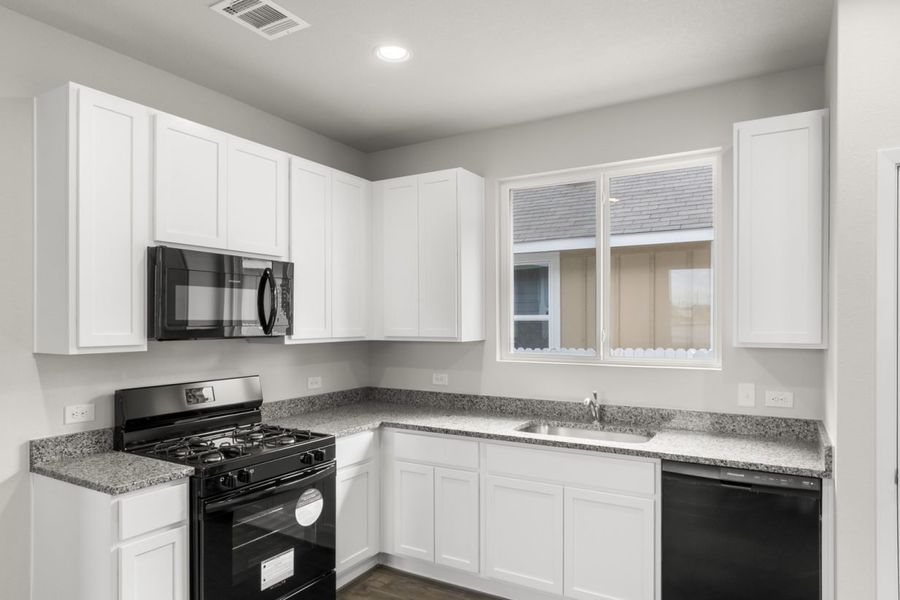 Image of a one story home kitchen with white cabinets and black appliances and a window above the sink
