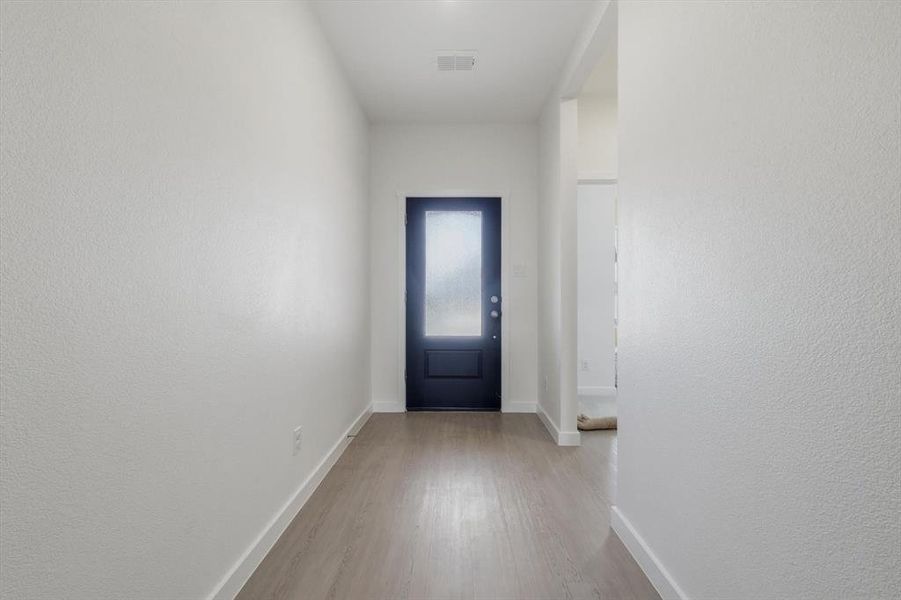 Entryway featuring a dark paneled door with frosted glass, wood-finish flooring, white baseboards, and neutral wall tones Entryway featuring a dark paneled door with frosted glass, wood-finish flooring, white baseboards, and neutral wall tones