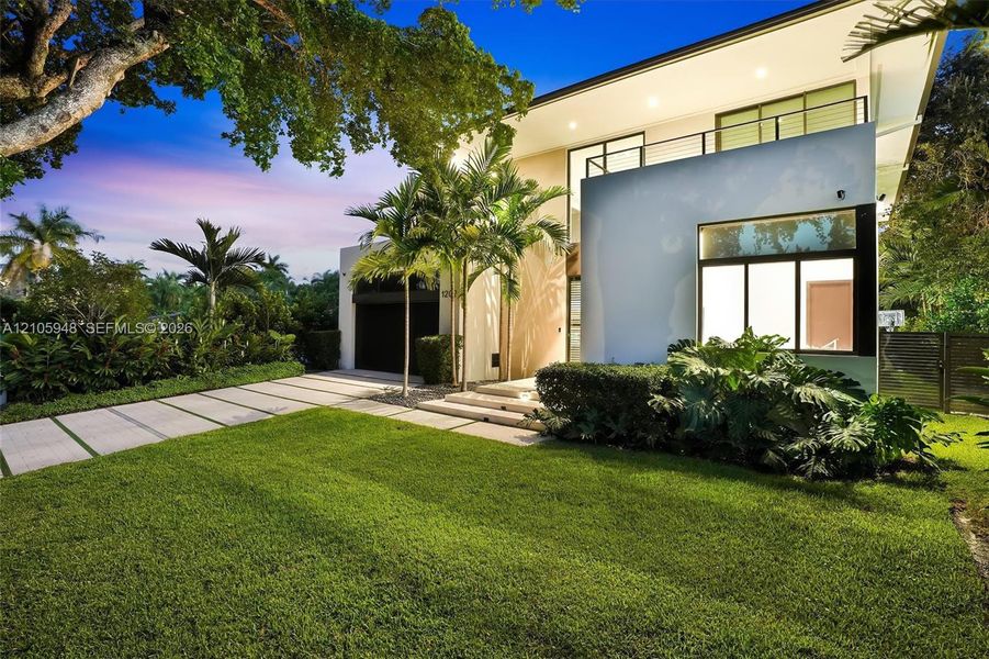 Modern two-story architectural exterior featuring smooth stucco finish, expansive glass windows, an upper-level balcony with metal railing, and a concrete paver driveway