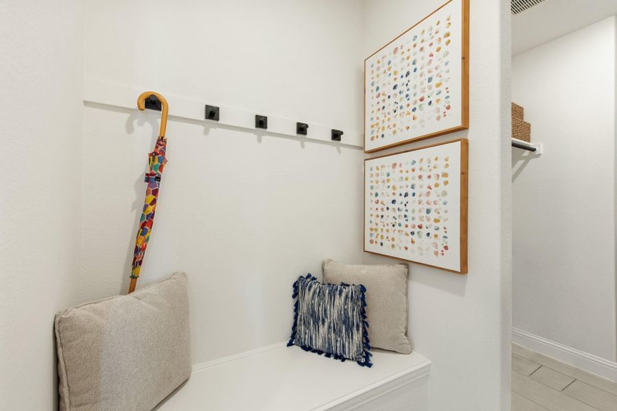 Mudroom nook with built-in bench, wall hooks, colorful umbrella, and two framed art pieces above seating. Mudroom nook with built-in bench, wall hooks, colorful umbrella, and two framed art pieces above seating.