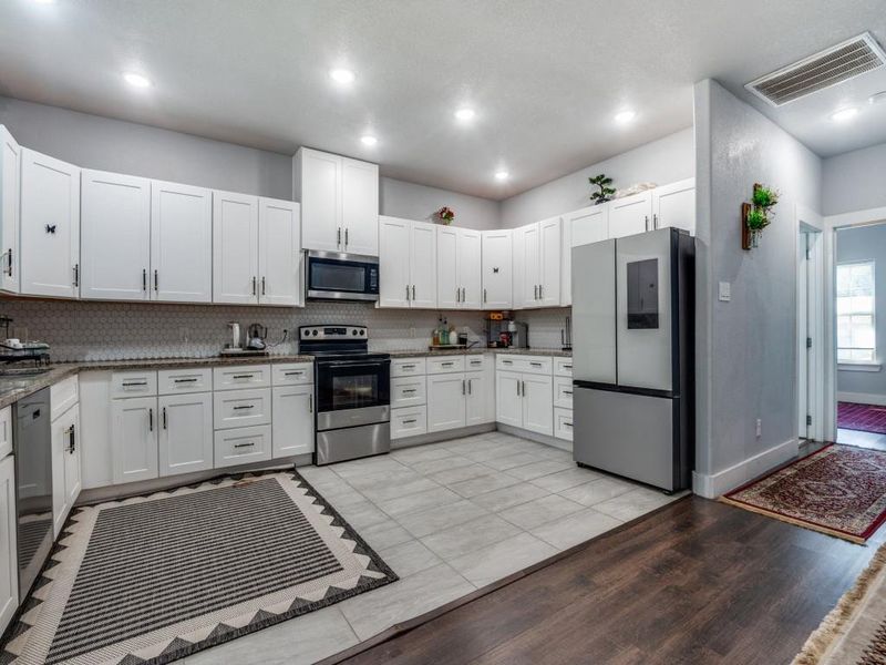 Kitchen with stainless steel appliances, white cabinets, dark stone counters, tasteful backsplash, and light tile patterned floors Kitchen with stainless steel appliances, white cabinets, dark stone counters, tasteful backsplash, and light tile patterned floors