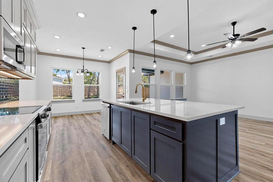 Kitchen with appliances with stainless steel finishes, hanging light fixtures, crown molding, light stone counters, and light wood finished floors