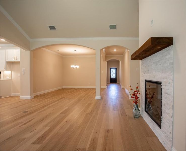 Unfurnished living room with an inviting chandelier, ornamental molding, a stone fireplace, and light wood-type flooring