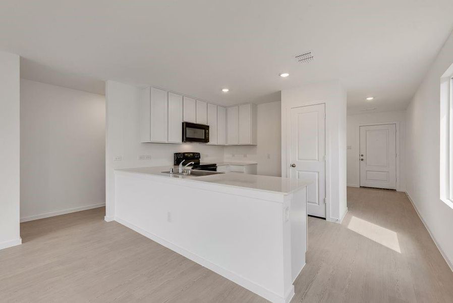 Kitchen with white cabinetry, a peninsula, light wood-style flooring, black appliances, and recessed lighting