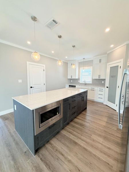 An inviting kitchen features a central island with an integrated microwave and chic pendant lighting.