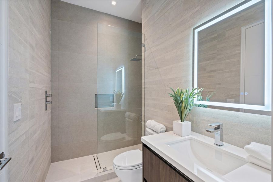Sleek modern bathroom with glass-enclosed shower, vanity, and illuminated LED mirror. Sleek modern bathroom with glass-enclosed shower, vanity, and illuminated LED mirror.