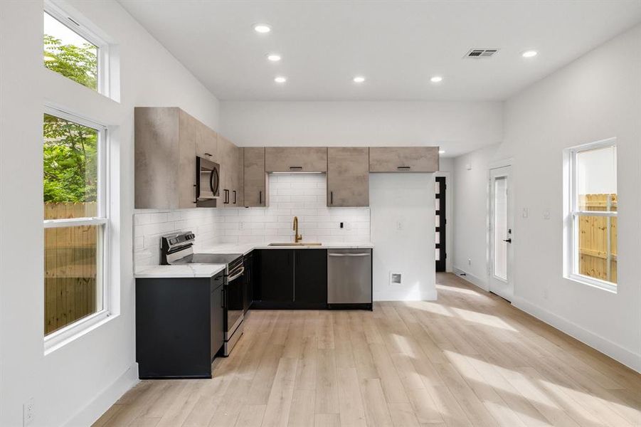 Kitchen with appliances with stainless steel finishes, light countertops, decorative backsplash, light wood-style floors, and recessed lighting