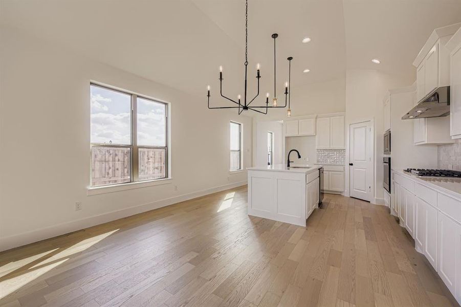 Kitchen featuring decorative backsplash, a chandelier, white cabinets, light wood-style flooring, and high vaulted ceiling Kitchen featuring decorative backsplash, a chandelier, white cabinets, light wood-style flooring, and high vaulted ceiling