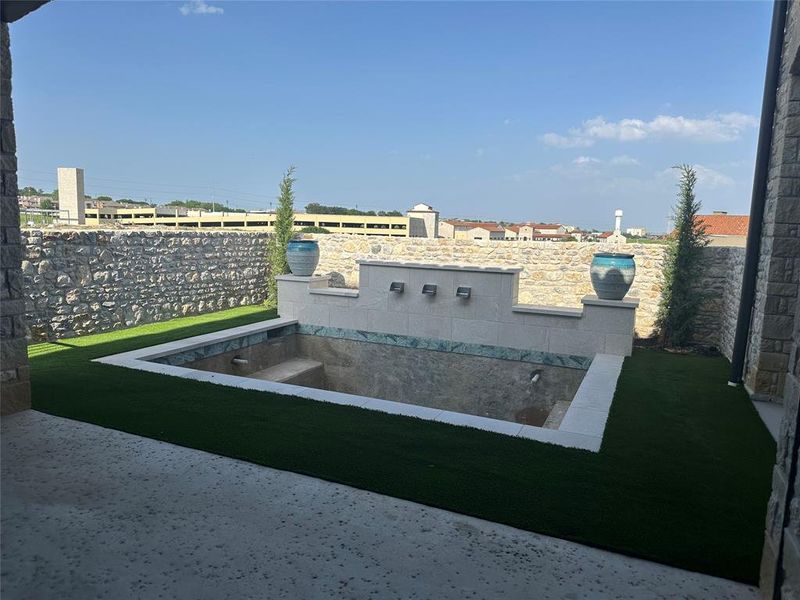 Pool will be plastered by May 15, 2026. This pool features waterfalls on back wall, and ledge seating on two sides of the pool. Pool is surrounded by turf. Flower pots will be filled with more landscaping once pool is complete.