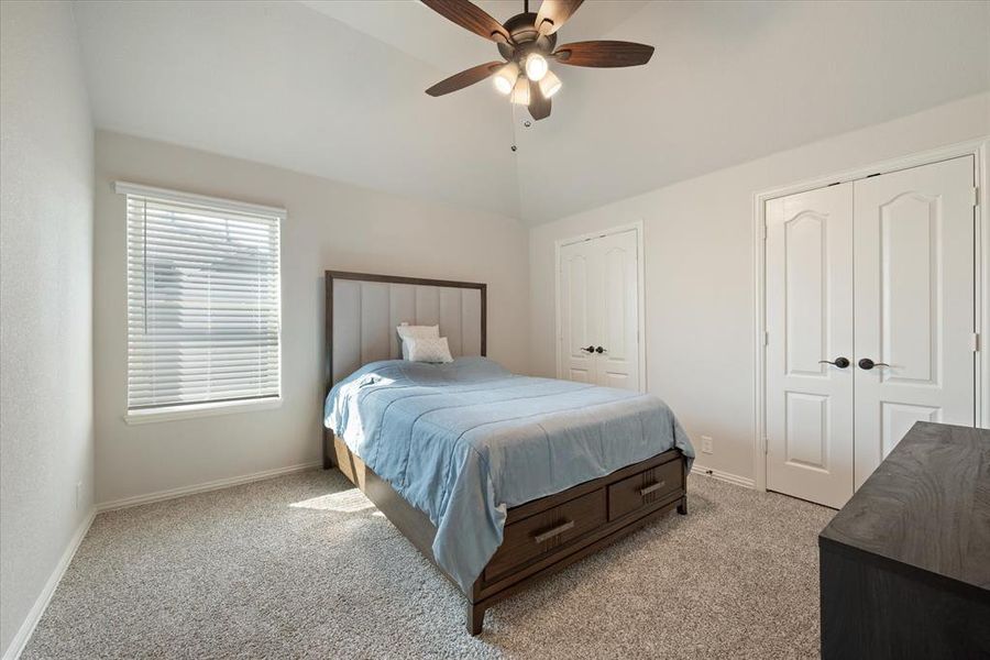 Upstairs secondary bedroom with light carpet, dual closets, lofted ceiling, and ceiling fan.