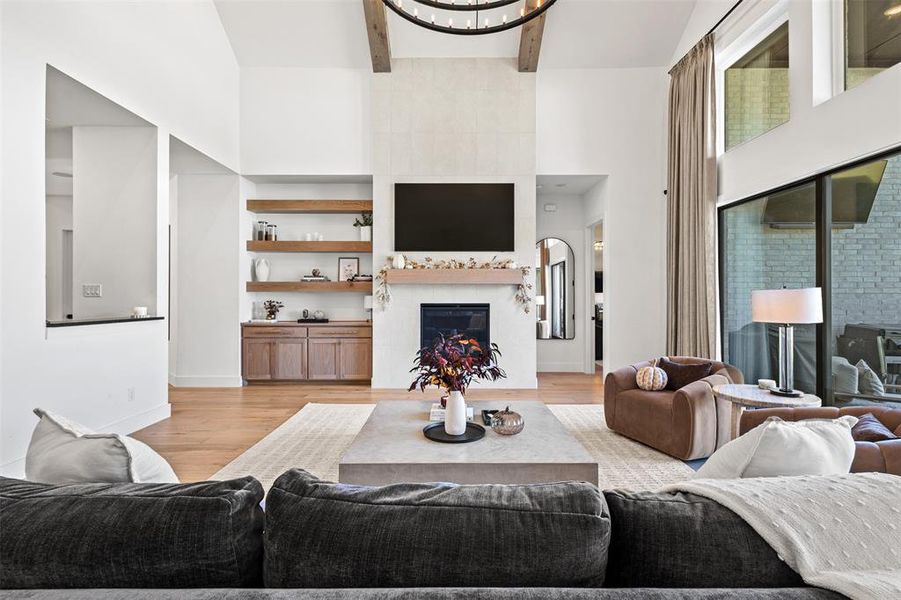 Living area with a large fireplace, light wood finished floors, beamed ceiling, a towering ceiling, and a chandelier Living area with a large fireplace, light wood finished floors, beamed ceiling, a towering ceiling, and a chandelier