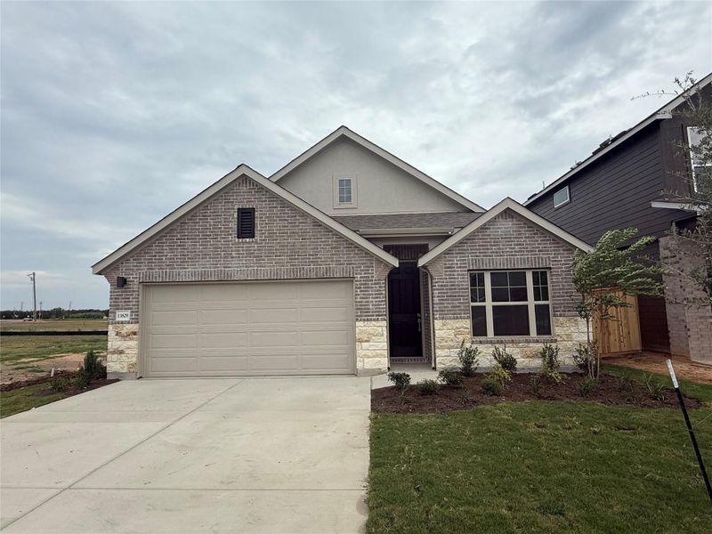 View of front of home featuring driveway, brick siding, a front yard, a garage, and stucco siding View of front of home featuring driveway, brick siding, a front yard, a garage, and stucco siding