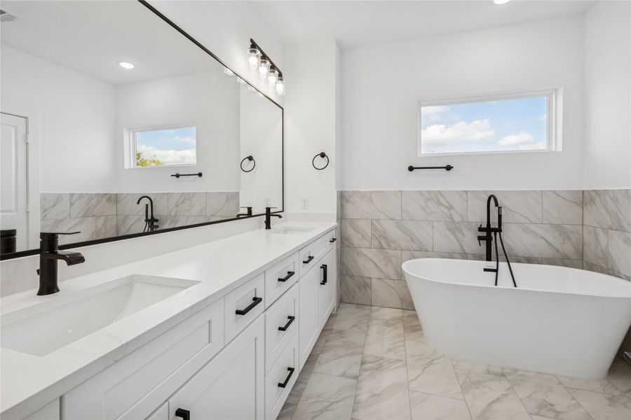 This bathroom features a sleek, modern design with a double vanity, black fixtures, a freestanding tub, and elegant marble tile accents, creating a luxurious and inviting space. This bathroom features a sleek, modern design with a double vanity, black fixtures, a freestanding tub, and elegant marble tile accents, creating a luxurious and inviting space.