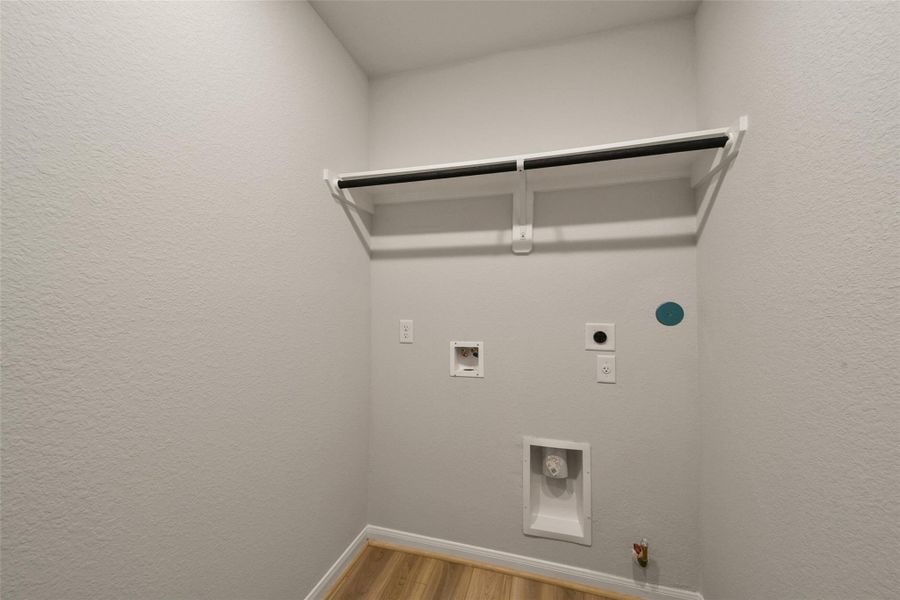 Functional laundry room featuring washer/dryer hookups, a convenient storage shelf, and a clean, light-toned aesthetic.
