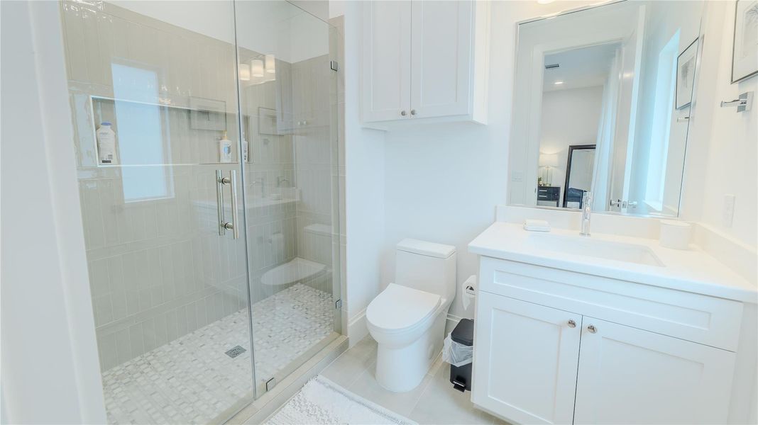 This photo showcases a bright, modern bathroom featuring a glass-enclosed shower with tile work, a sleek white vanity with ample storage, and a large mirror. The room is well-lit and exudes a clean, airy feel.