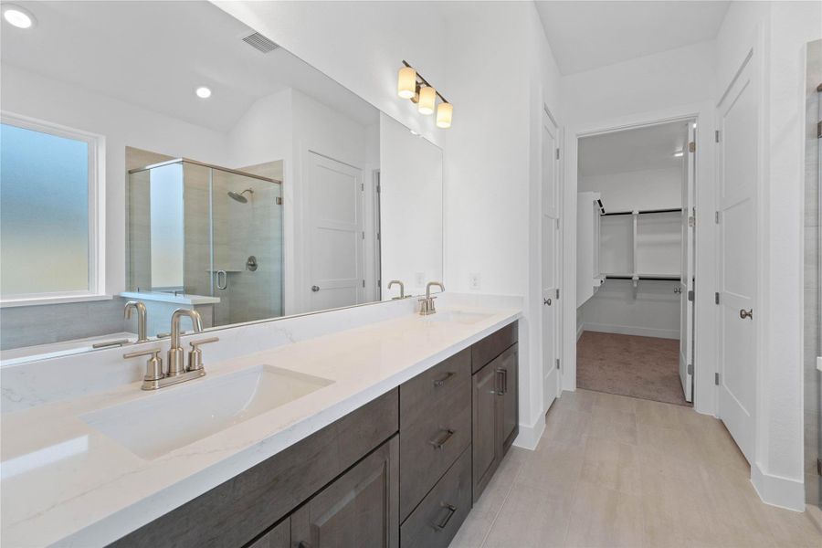 This stunningly updated primary bathroom is truly move-in ready! It features stained cabinetry with light countertops, dual vanities, a large mirror, a generous walk-in closet with built-in shelving, soaring ceilings, custom paint, and sleek modern finishes throughout.