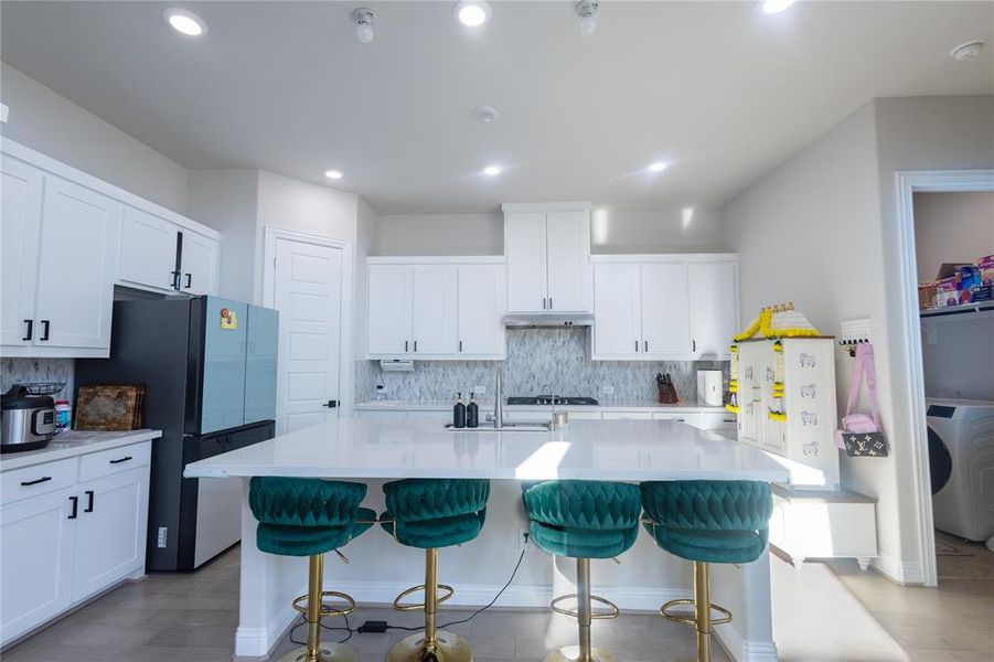 Kitchen featuring a breakfast bar area, white cabinetry, tasteful backsplash, freestanding refrigerator, and a kitchen island with sink