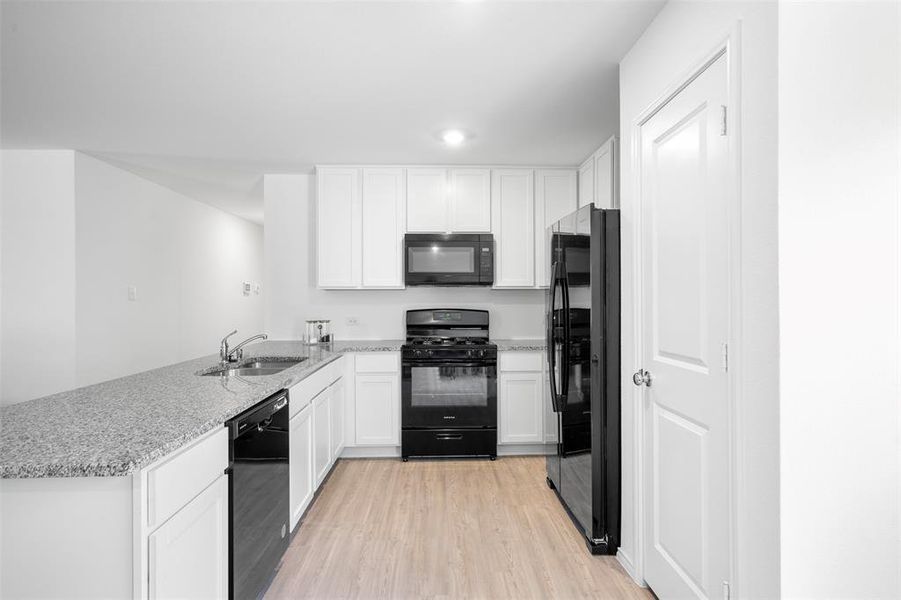 Kitchen with black appliances, light wood finished floors, white cabinetry, a peninsula, and light stone counters Kitchen with black appliances, light wood finished floors, white cabinetry, a peninsula, and light stone counters