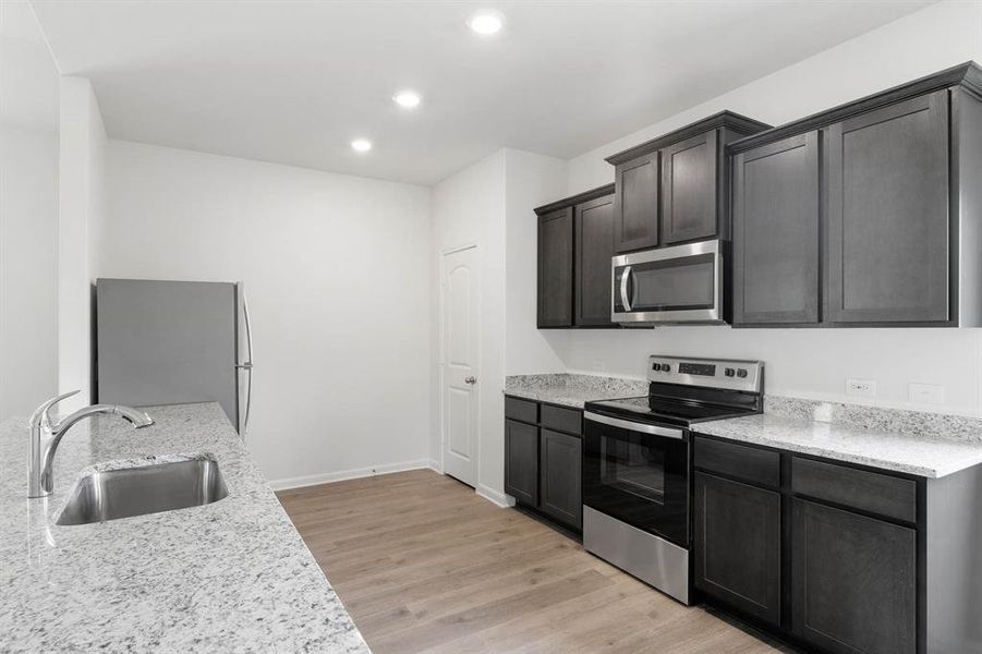 Kitchen with sink, stainless steel appliances, light wood-style flooring, and light stone countertops