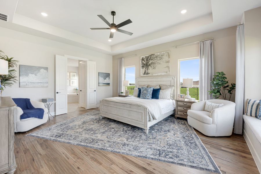 Spacious master bedroom with tray ceiling, ceiling fan, hardwood floors, and large area rug
