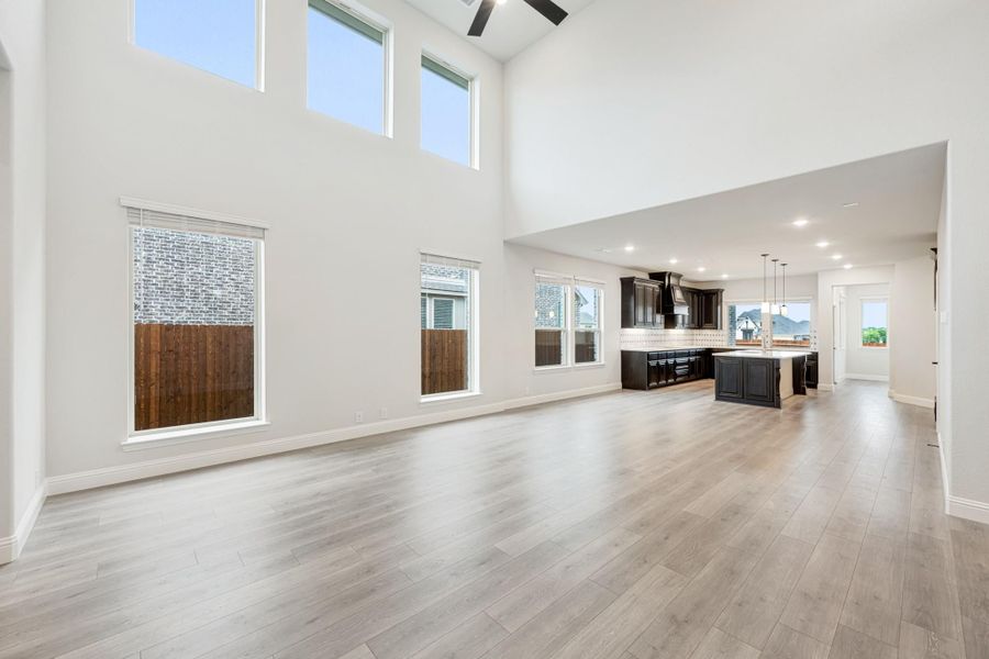 Open living area with two-story ceiling, hardwood floors, and open-concept kitchen with dark cabinets in background