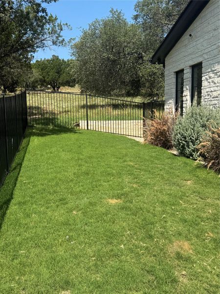 A well-kept lawn borders a modern home, leading to a fenced-in yard with mature trees.
