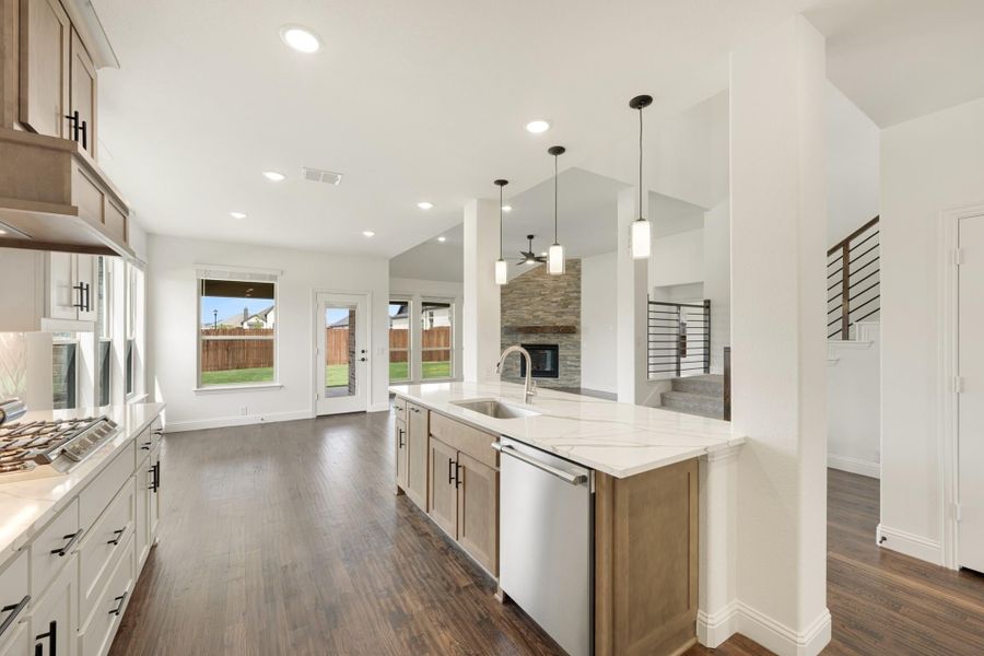 Open-concept kitchen with center island, quartz countertops, and dark hardwood floors opening to living area with stone fireplace.
