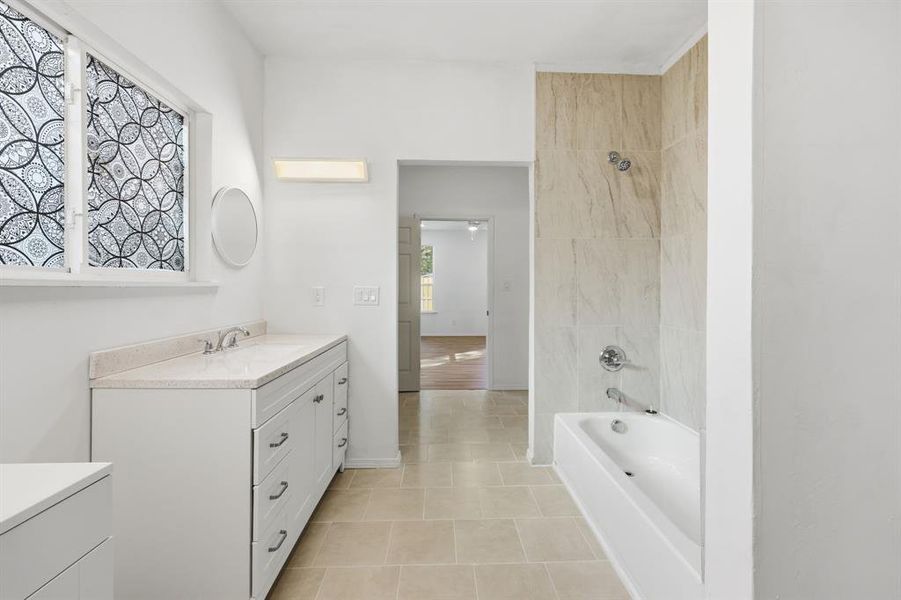 Primary ensuite bathroom with dual vanities, separate tub and shower and light tile patterned floors