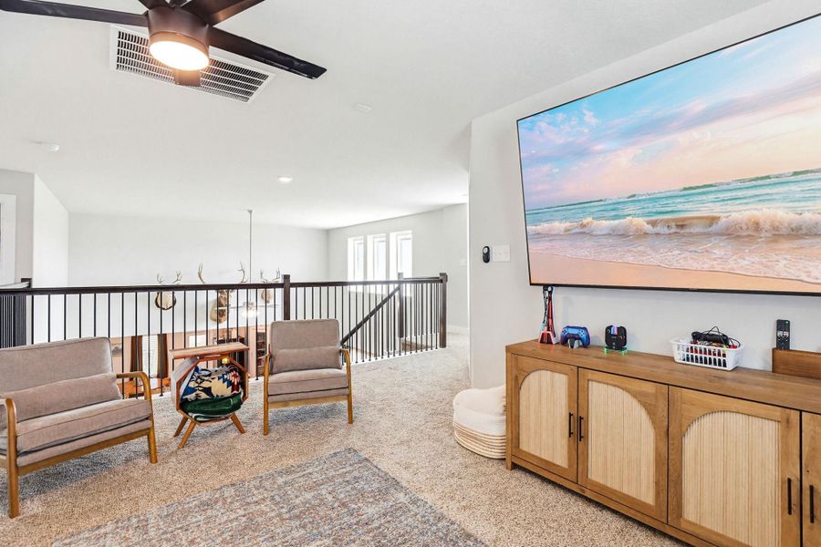 Carpeted loft area featuring a ceiling fan, black metal railing, and a media console with natural wood-tone finishes