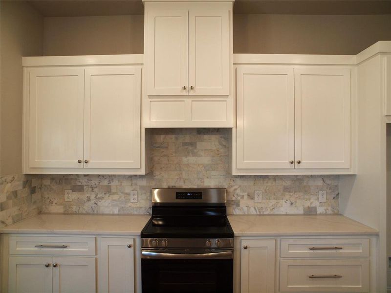 Kitchen with white cabinetry, backsplash, and stainless steel electric stove