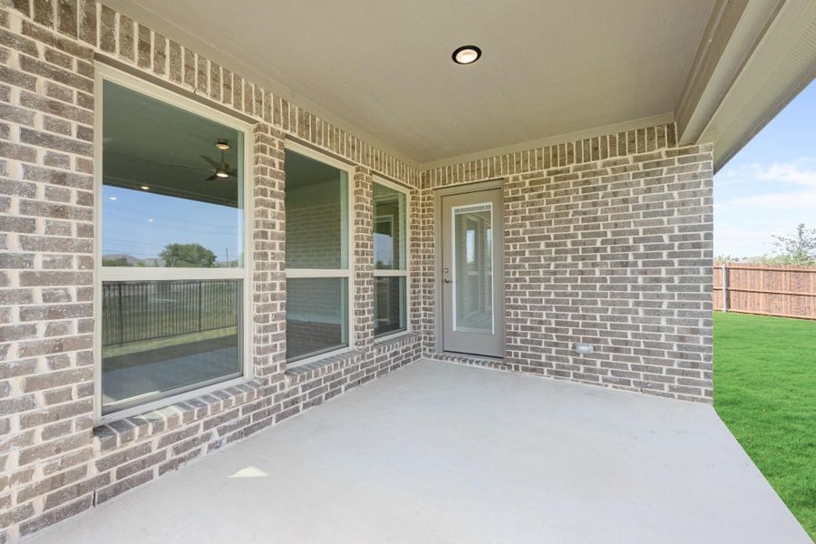 Covered back patio with concrete floor, brick exterior, back door, and fenced green lawn.