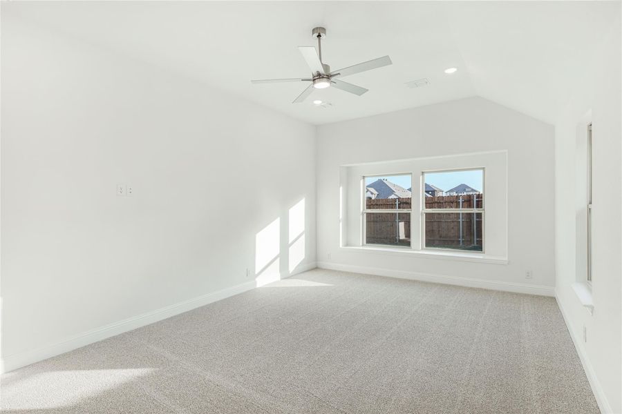 Empty bedroom with vaulted ceiling, ceiling fan, carpet flooring, and a double window overlooking a backyard fence