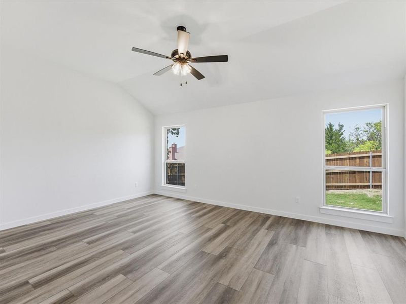 Spacious room featuring vaulted ceilings, wood-finish flooring, white walls, two large windows, and a ceiling fan with integrated lighting Spacious room featuring vaulted ceilings, wood-finish flooring, white walls, two large windows, and a ceiling fan with integrated lighting